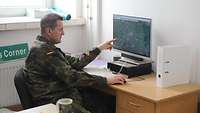 Ein Soldat sitzt vor einem Computer und zeigt auf den Bildschirm. 