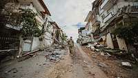 Ein Soldat läuft eine Straße entlang an Trümmern und zerstörten Häusern vorbei.