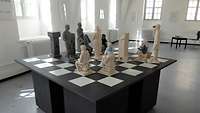Ein überdimensionales Schachbrett mit schwarzen und weißen Figuren in einem Raum.