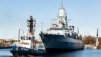 Die Fregatte Hamburg von seitlich vorn mit einem Schlepper vor ihr