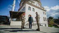Zwei Soldaten stehen mit einem Mann vor einer Moschee