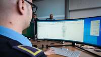 Mann in blauer Uniform arbeitet vor einem Computer-Bildschirm.