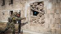 Zwei Soldaten stehen vor einer Hauswand. Einer wirft eine blaue Übungsgranate in ein Fenster.