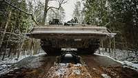 Ein Pionierpanzer Dachs fährt über eine Schnellbrücke in einem verschneiten Wald.