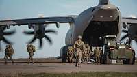 Aus einem Flugzeug auf einem Flugplatz steigen Soldaten. Material wird mit Maschinen abgeladen. 
