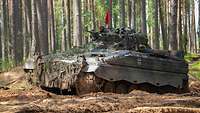 Ein Schützenpanzer „Marder“ fährt durch ein Übungsgelände im Wald. Der Panzer ist mit einer roten Flagge versehen.