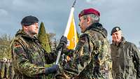 Ein Soldat übergibt an einen anderen Soldaten eine gelb-weiße Fahne.