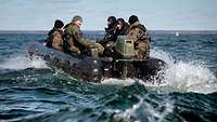 Fünf Soldaten in Flecktarn sitzen in einem schwarzen Gummiboot und fahren auf einem See mit Wellen.