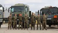 Sieben Soldaten in Flecktarnuniform stehen nebeneinander vor drei großen Tankfahrzeugen der Bundeswehr.
