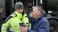 Ein deutscher Soldat und ein polnischer Zivilist stehen vor einem polnischen Tankfahrzeuges und schauen auf ein Handy.