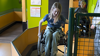 Ein Mädchen sitzt in einem Rollstuhl und versucht ein Hindernis zu überwinden. 