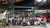 Eine Besuchergruppe hat sich vor einer Dampflokomotive zum Gruppenbild aufgestellt.