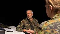 Ein Soldat sitzt in einem dunklen Raum auf einem Stuhl und gibt ein Interview.