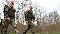 Zwei Soldaten marschieren mit Schutzweste und in Flecktarnuniform auf einem Waldweg.