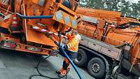 Ein Mann mit orangener Arbeitsbekleidung flanscht einen Schlauch an einen Lkw-Aufbau