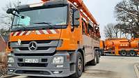 Ein orangener Lkw mit Spezialaufbauten, im Hintergrund ein weiterer