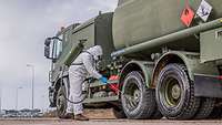 Ein Soldat mit Ganzkörperanzug sprüht einen Tankwagen mit einer Flüssigkeit ab