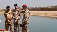 Ein deutscher Soldat erklärt zwei irakischen Soldaten etwas. Im Hintergrund ein Wasserbecken.