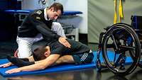 Ein Soldat unterstützt eine männliche Person bei einer Physiotherapieübung