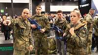Eine Gruppe junger Menschen in Uniform. Ein Soldat zeigt zum Betrachtenden, die Gruppe hört zu.