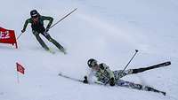 Zwei Skifahrende nehmen eine enge Kurve, dabei rutscht einer aus und stürzt.