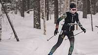 Eine Langläuferin fährt mit einer Kartenhalterung vor dem Körper durch den Wald