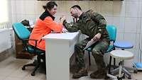 Eine polnische Sanitäterin in oranger Jacke schlägt einen Soldaten beim Armdrücken.
