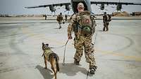 Ein Soldat mit Hund an der Leine läuf auf das Transportflugzeug A400M mit geöffneter Heckklappe zu