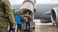 Menschen bilden eine Schlange an einer rollbaren Treppe und steigen in ein Flugzeug ein.