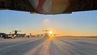 Zu sehen sind mehrere Transportflugzeuge auf einem Rollfeld, mit untergehende Sonne im Hintergrund.