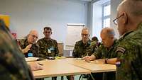 Several soldiers sitting around a table, talking to each other.