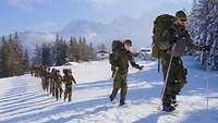 Eine Gruppe von Soldaten läuft in einer Linie mit Schneeschuhen und Skistöcken.