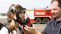 Ein Feuerwehrmann hilft einem Mädchen beim Anlegen einer Atemschutzmaske