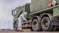 Ein ABC-Abwehrsoldat in Schutzanzug sprüht einen Tankwagen der Bundeswehr ab
