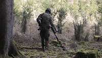 Ein Soldat durchstreift mit einem Metalldetektor den Wald