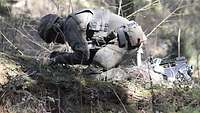 Ein Soldat kniet auf einen Waldboden und gräbt etwas aus