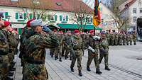 Soldatinnen und Soldaten laufen in Formation auf dem Marktplatz und tragen die Truppenfahne