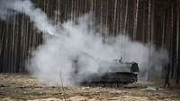 Eine Panzerhaubitze in Rauch gehüllt steht auf einer Lichtung im Wald.