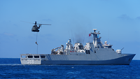 Eine Person seilt sich von einem Hubschrauber auf ein Kriegsschiff in See ab.