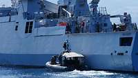 Soldaten steigen von einem Schlauchboot über eine Leiter auf ein Kriegsschiff in See.