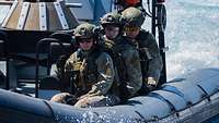Drei Soldaten sitzen auf der linken Seite eines Speedboates.
