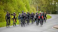 Eine Gruppe von Fahrradfahrern in schwarzer Kleidung fährt gesammelt auf einer Straße.