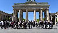 Viele Radfahrer stehen neben ihren Rädern in einer Reihe vor dem Brandenburger Tor in Berlin bei bestem Wetter.