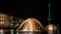 Beleuchteter Springbrunnen bei Nacht, dahinter ein Gebäude und der Funkturm grünleuchtend