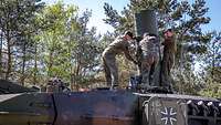 Auf einem Panzer in einem Wald stehen drei Soldaten und bringen ein Rohr auf einer Luke an.