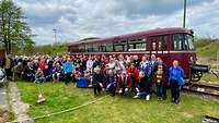 Eine große Menschengruppe hat sich vor einem alten dunkelroten Schienenbus aufgestellt. 