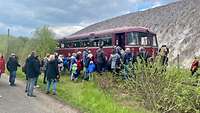 Menschen steigen in einen historischen dunkelroten Schienenbus.