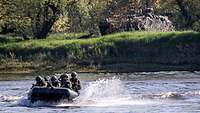 Bewaffnete Soldaten fahren mit einem Schlauchboot schnell über einen Fluss.