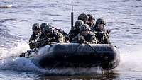 Soldaten mit Waffen im Anschlag fahren mit einem Schlauchboot schnell über einen Fluss.