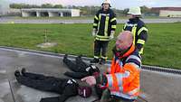 Der Sanitäter weist zwei Feuerwehrleute an weitere Puppen um ihn herum zu positionieren.